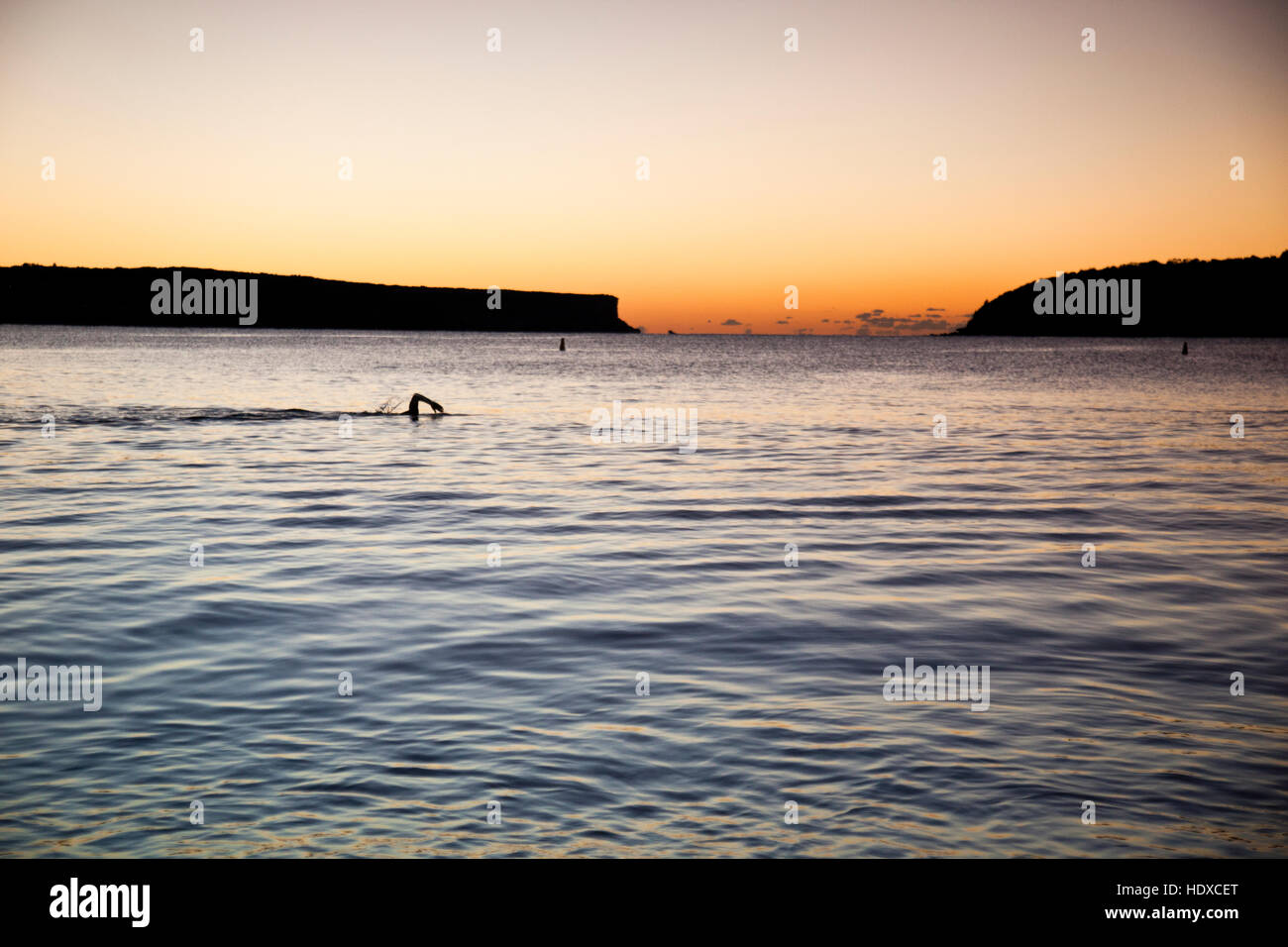 Arm of a swimmer comes out of the water mid-stroke swimming in the sea before sunrise Stock Photo
