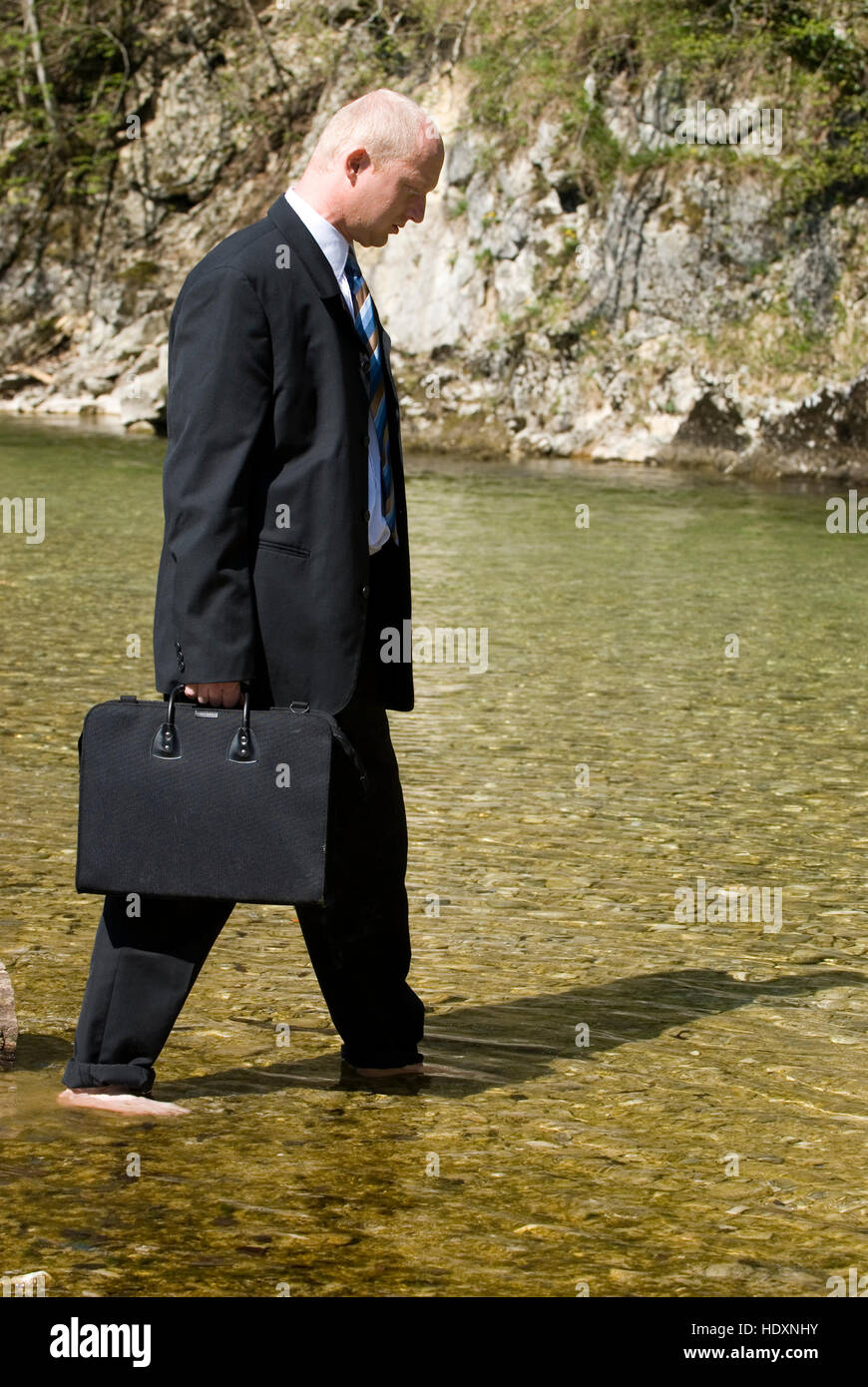 Businessman walking through a mountain brook Stock Photo