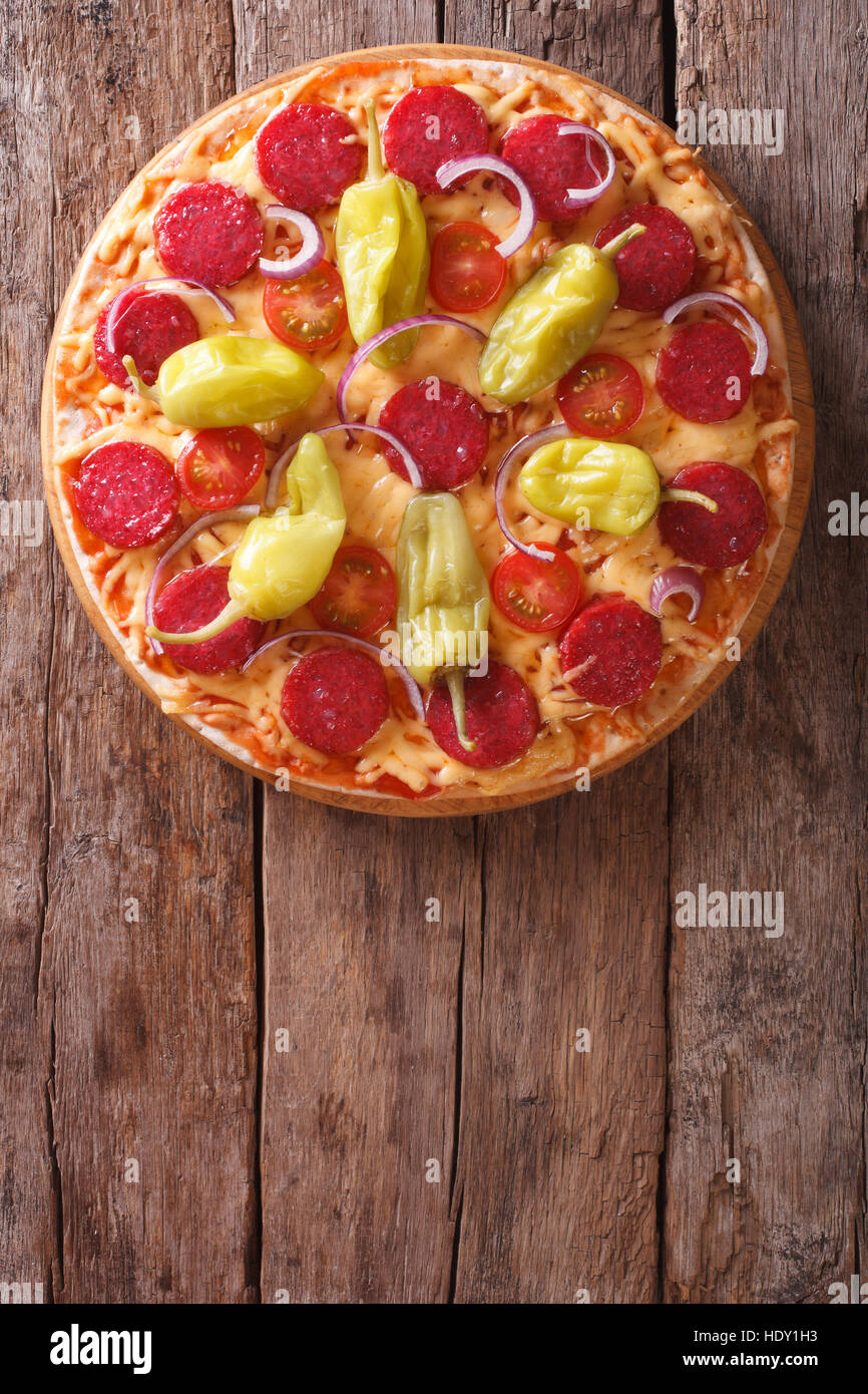 Italian pizza with salami, pepperoni pepper and tomatoes on a table close-up vertical view from above, rustic style Stock Photo
