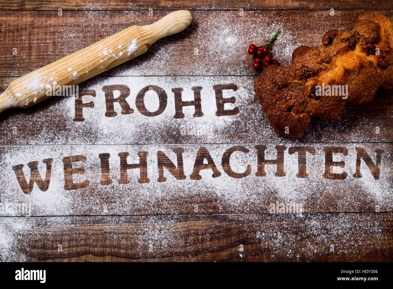 high-angle shot of a wooden table sprinkled with icing sugar or flour where you can read the text frohe weihnachten, merry christmas in german, a roll Stock Photo