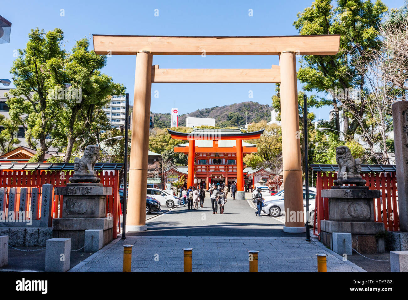 Wooden torri gate over road leading to bright vermillion torii and gatehouse, mon at the Shinto Ikuta shrine, Kobe in Japan. Stock Photo