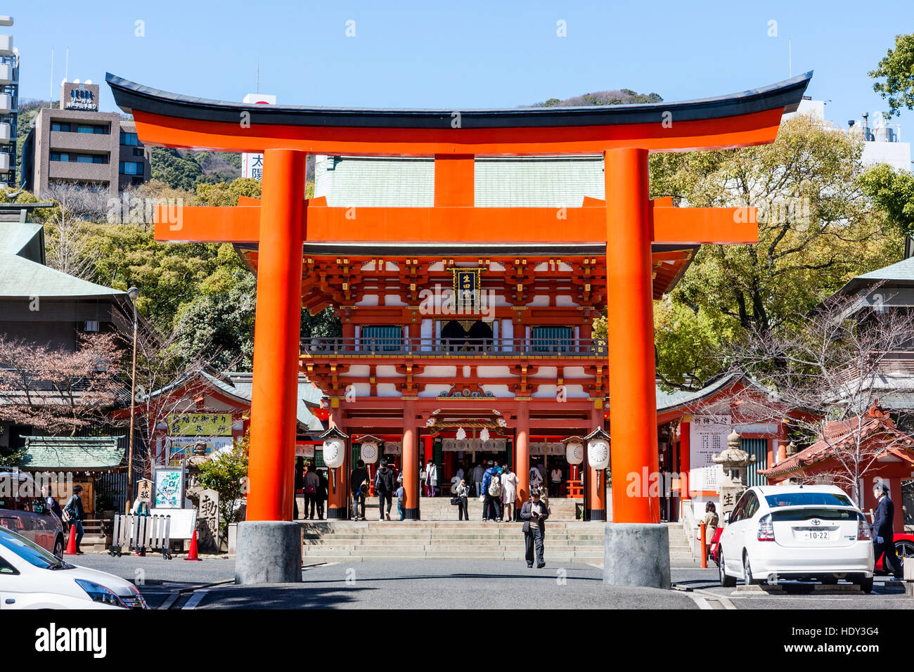 Japan, Kobe, Ikuta Shinto shrine. Vermillion torri gate across entrance, with gatehouse, mon, behind. Bright sunshine. Blue sky. Stock Photo
