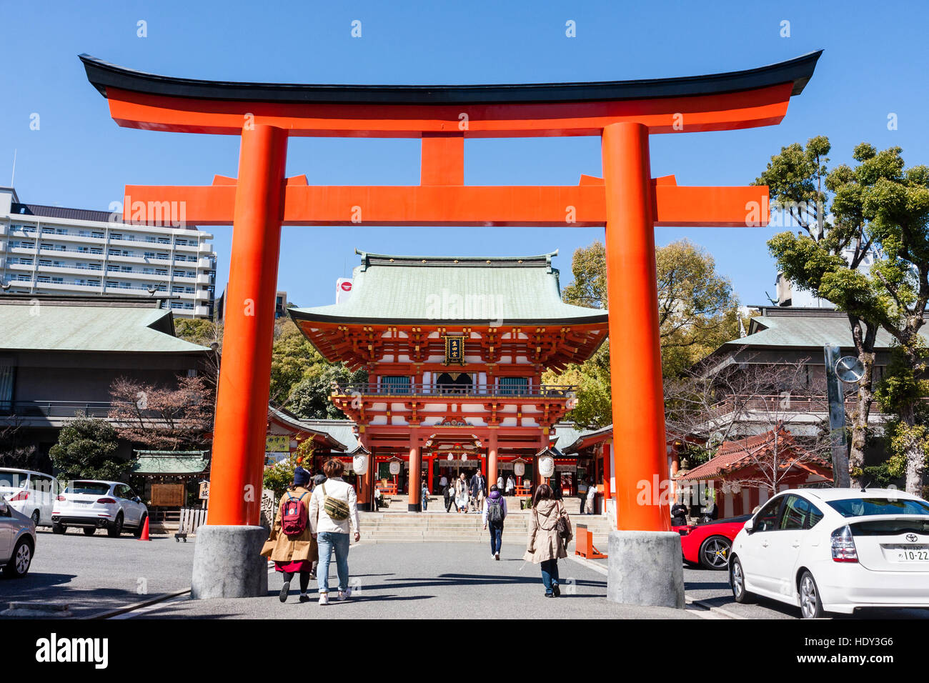Japan, Kobe, Ikuta Shinto shrine. Vermillion torri gate across entrance, with gatehouse, mon, behind. Bright sunshine. Blue sky. Stock Photo