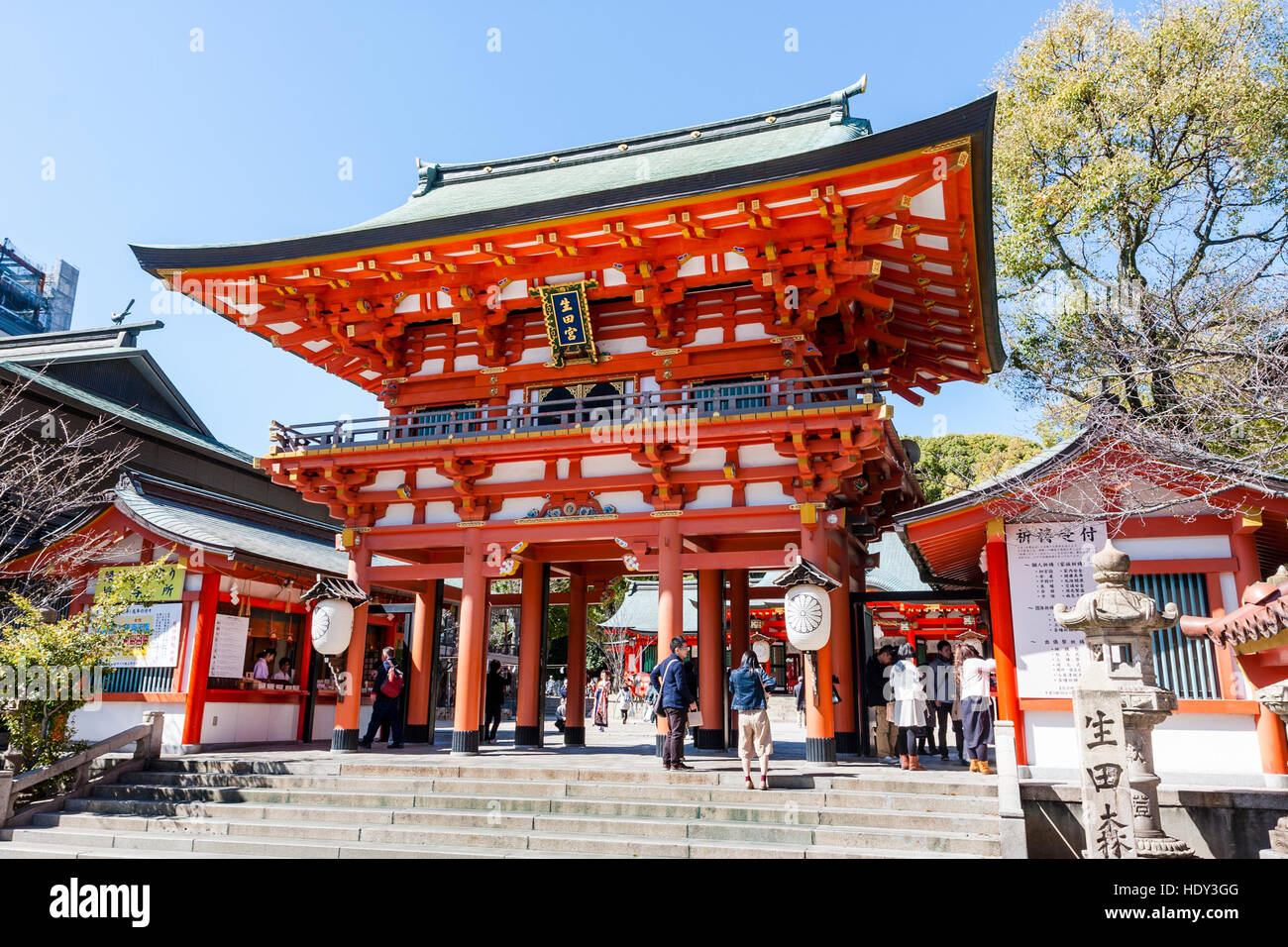Japan, Kobe, Ikuta shrine. Ikuta-jinja. Two storey vermilion mon, gate, entrance to shrine. People walking through. Bright sunshine, blue sky. Stock Photo