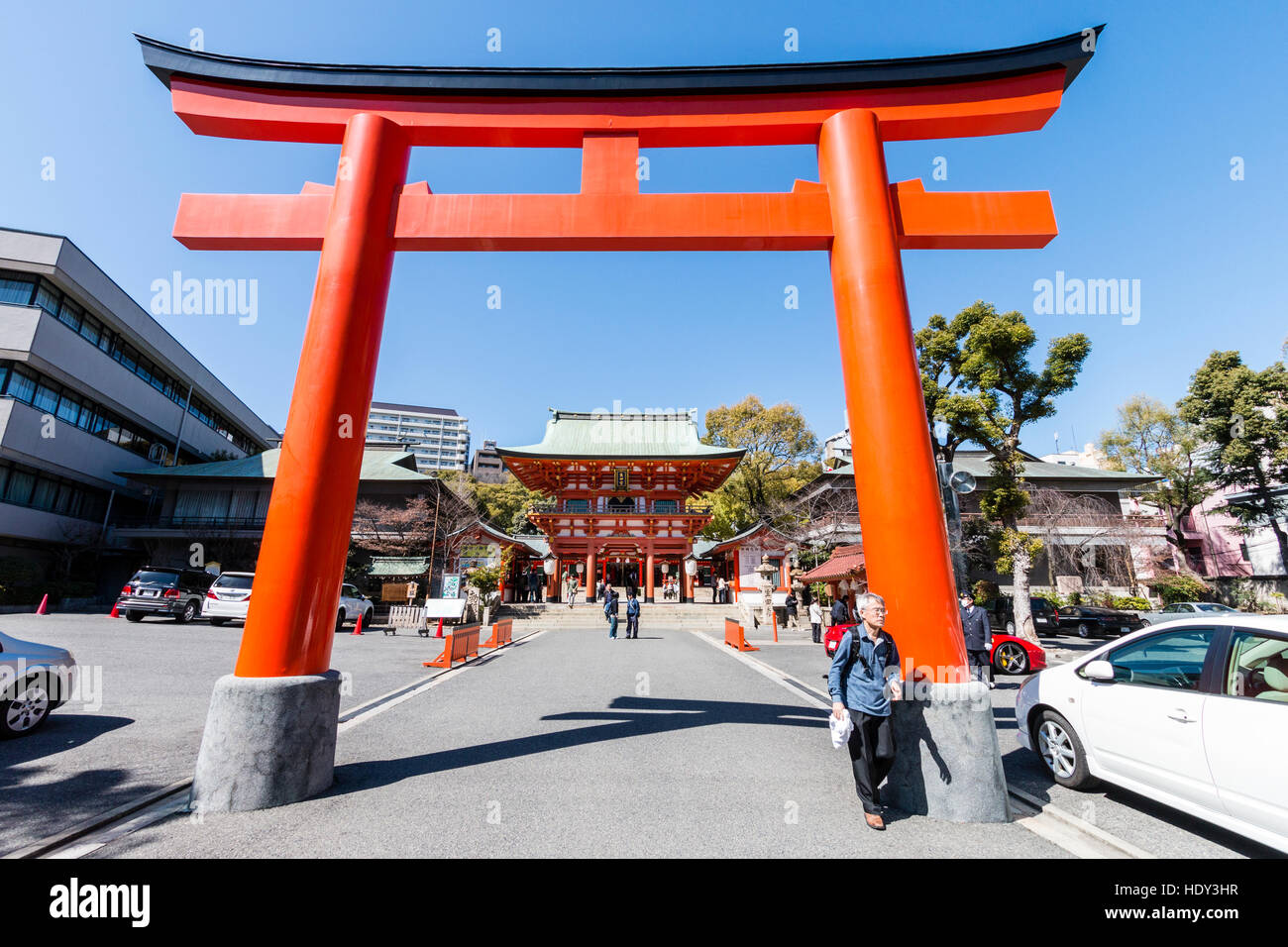 Japan, Kobe, Ikuta Shinto shrine. Vermillion torri gate across entrance, with gatehouse, mon, behind. Bright sunshine. Blue sky. Stock Photo