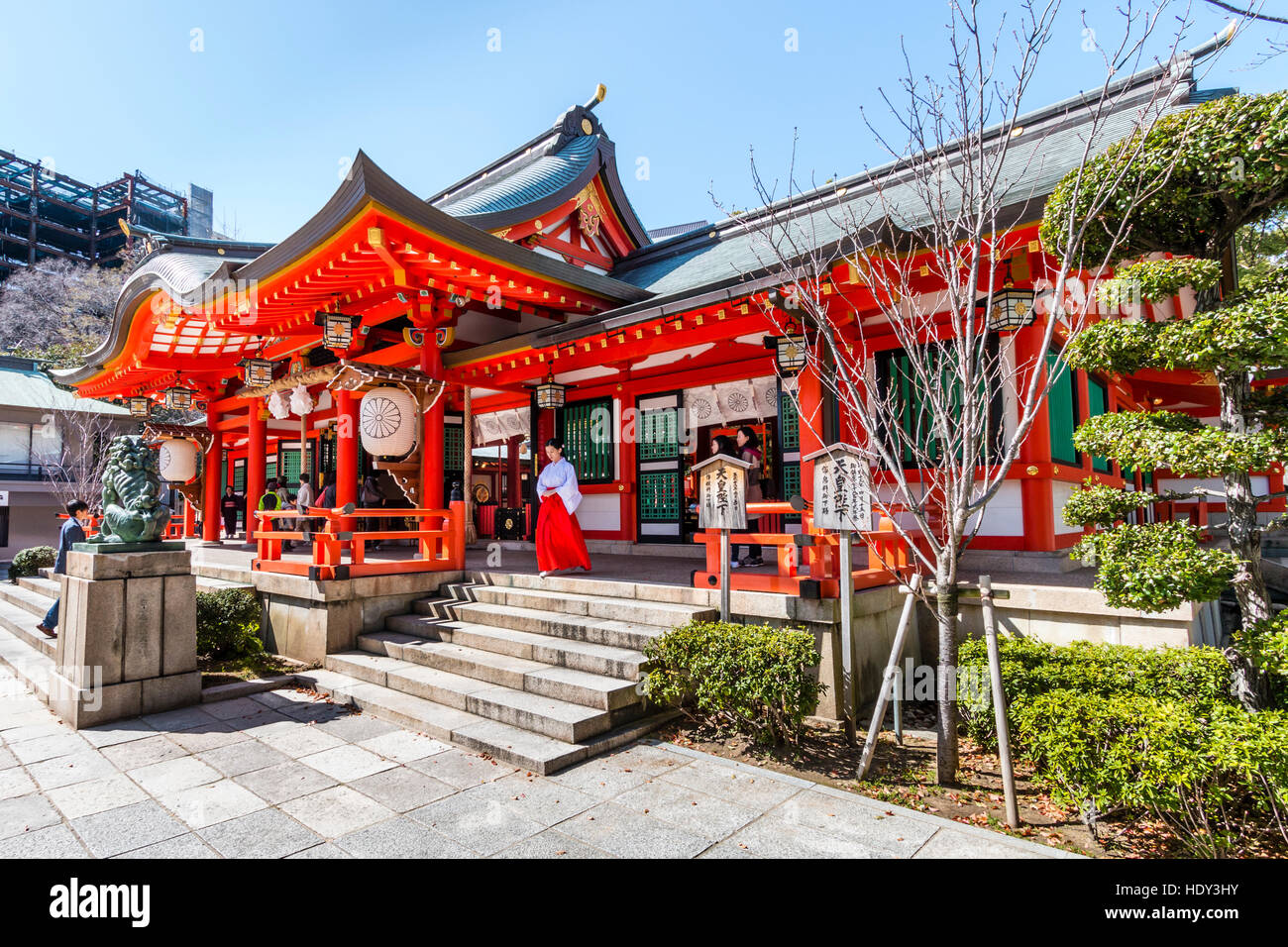 Popular Shinto Ikuta shrine in Kobe, Japan. Vermillion main hall, Honden,  with shrine maiden, miko, walking out. Bright sunshine, blue sky Stock  Photo - Alamy