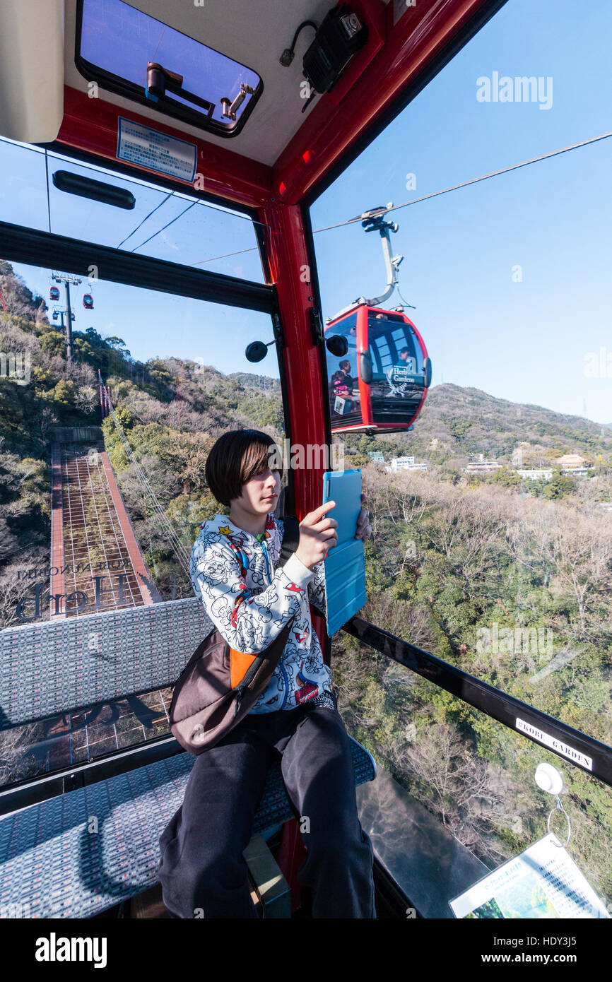Japan, Kobe. Caucasian young male teenager, 14-15 years old, in cable car on Shin-ropeway, while filming the journey with an I-pad, tablet. Stock Photo