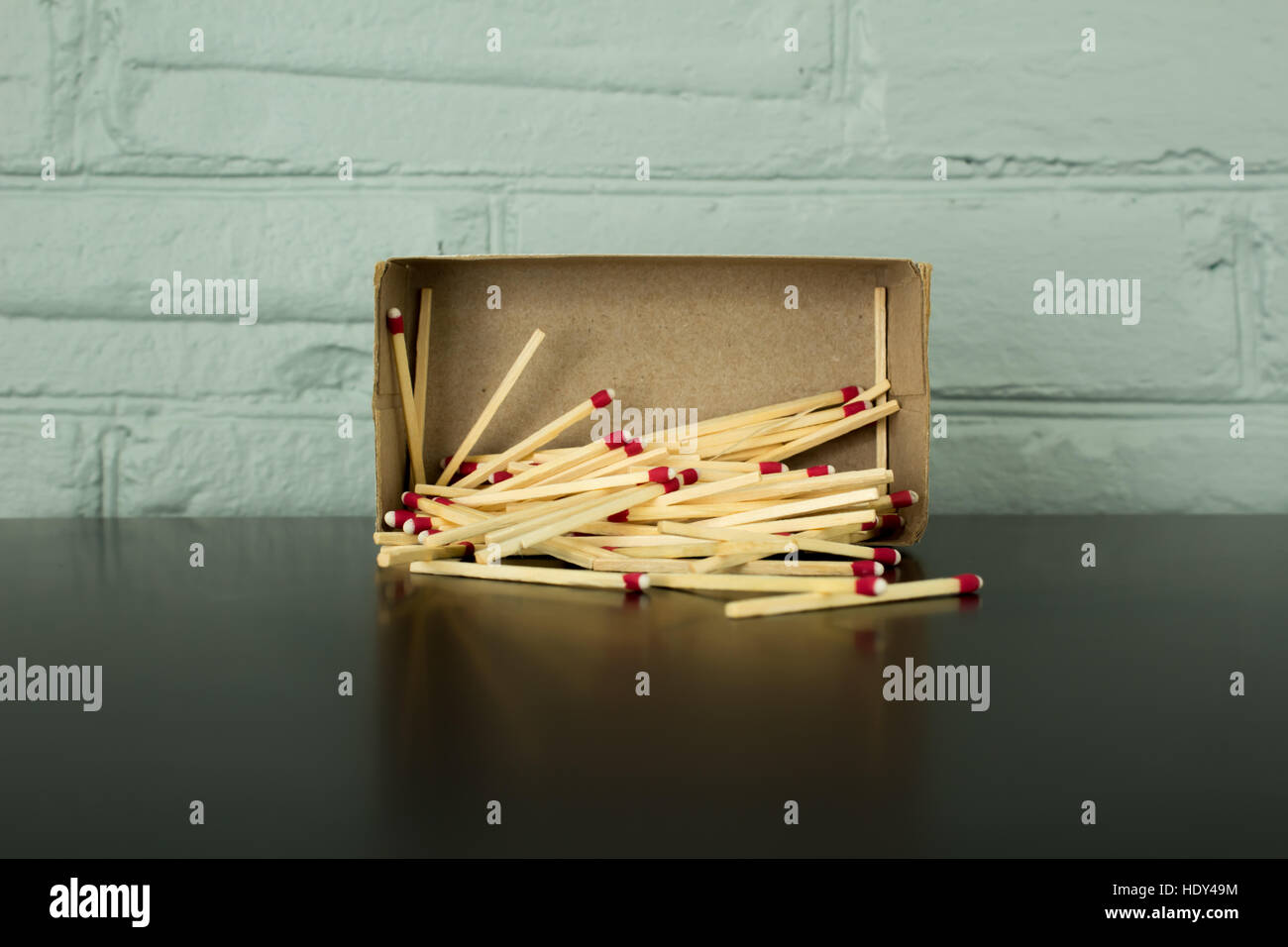 Strike-anywhere matches spilling out of matchbox against a blue painted brick background, with reflection on black table. Stock Photo