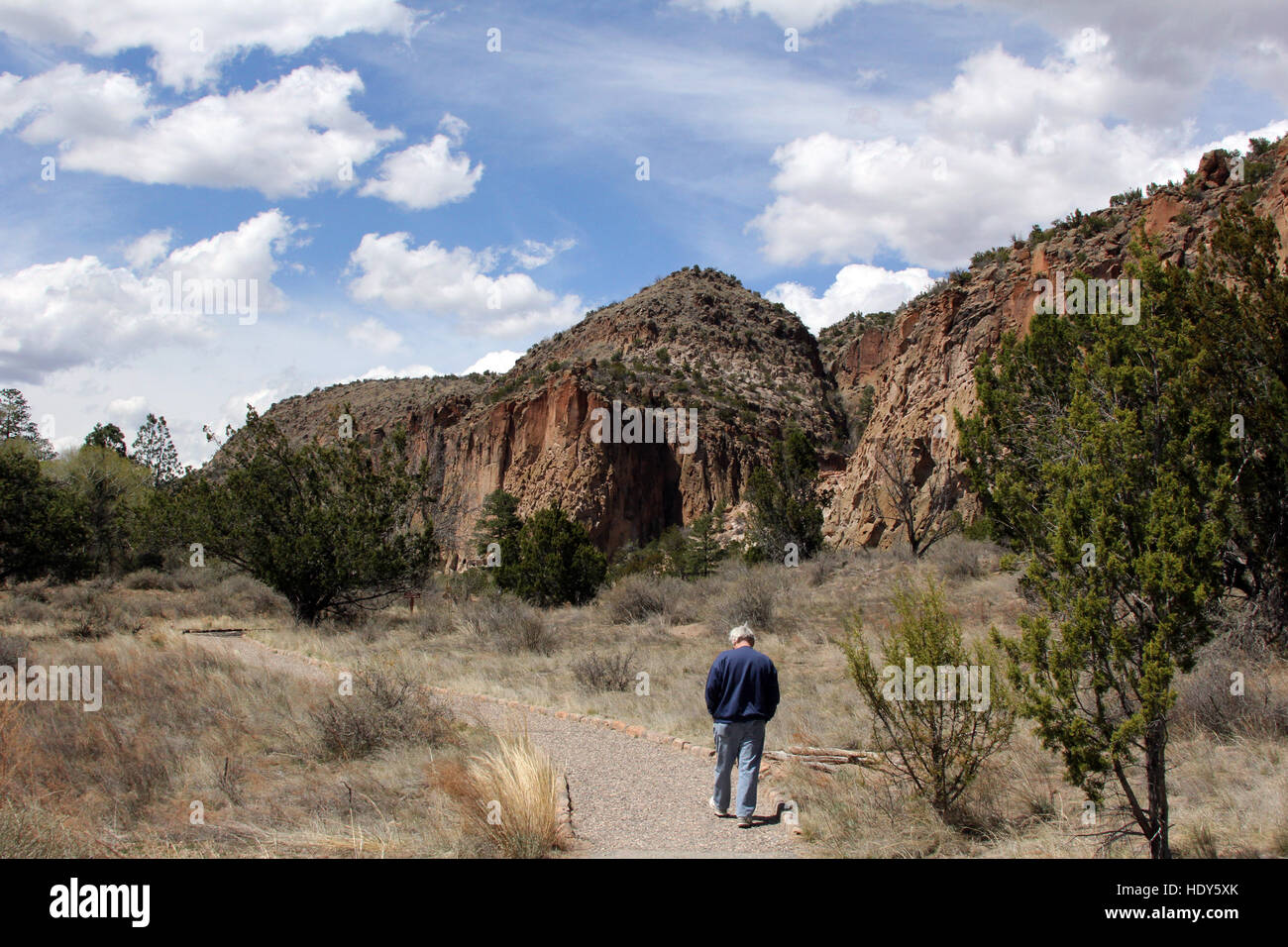 Man walks the main trail, crossing a river, then leading to the ancient cliff dwellings of Bandelier National monument. Stock Photo