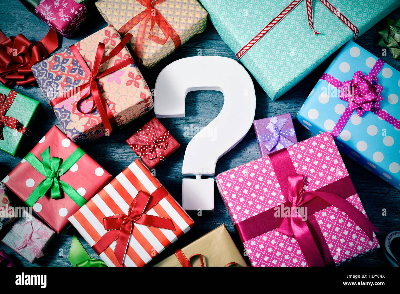 high-angle shot of many gifts wrapped in nice papers and tied with ribbons of different colors and a white three-dimensional question tag in the cente Stock Photo