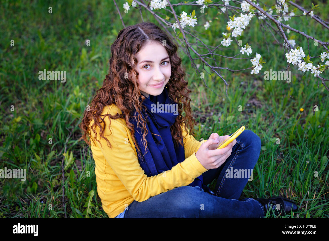 beautiful young woman sitting on the grass with phone Stock Photo