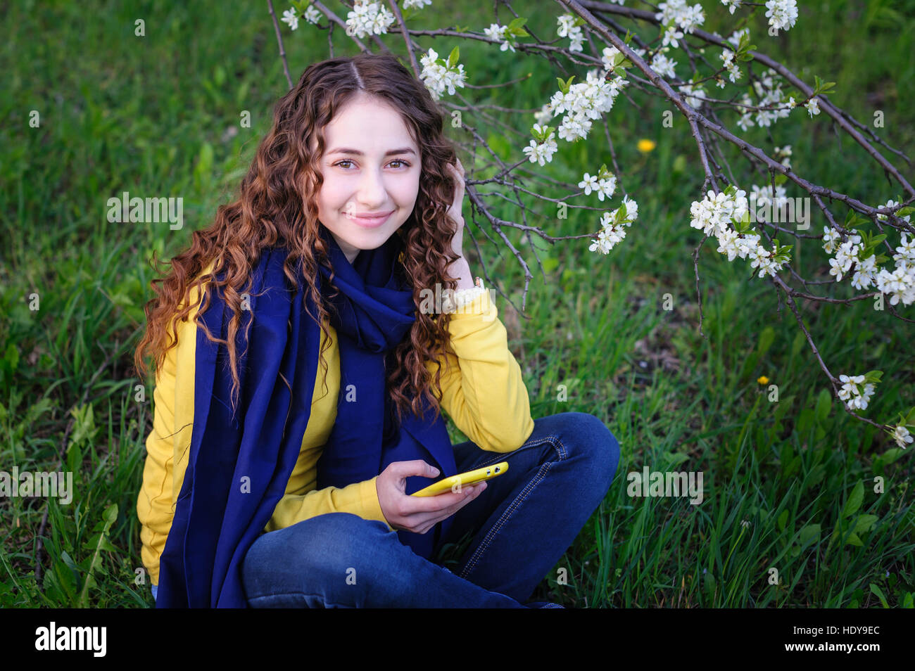 beautiful young woman sitting on the grass with phone Stock Photo