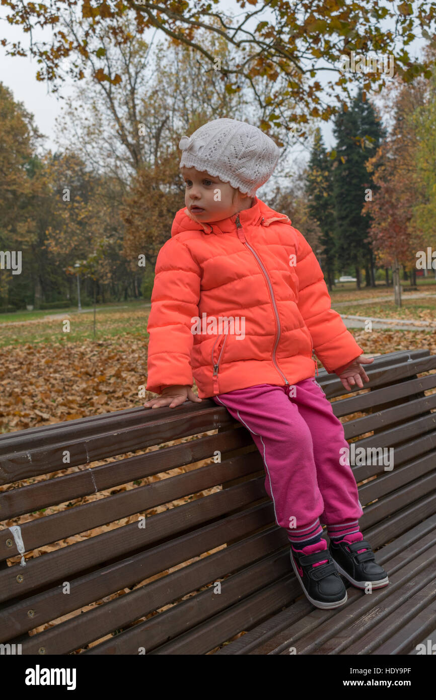 Little girl sitting on the bench in the park. Autumn in the park Stock ...