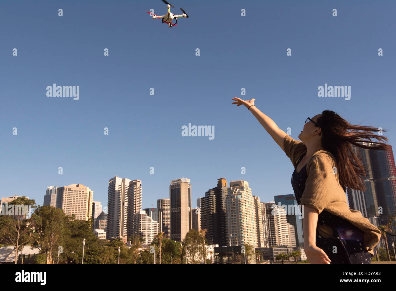A young woman playing and launching with a small drone in a park near city buildings Stock Photo