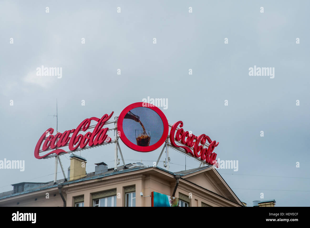 BELARUS, MINSK - AUGUST 17, 2016:  neon signage with some famous brand - COCA COLA. Ad in city centrum stand above building on roof against blue sky Stock Photo