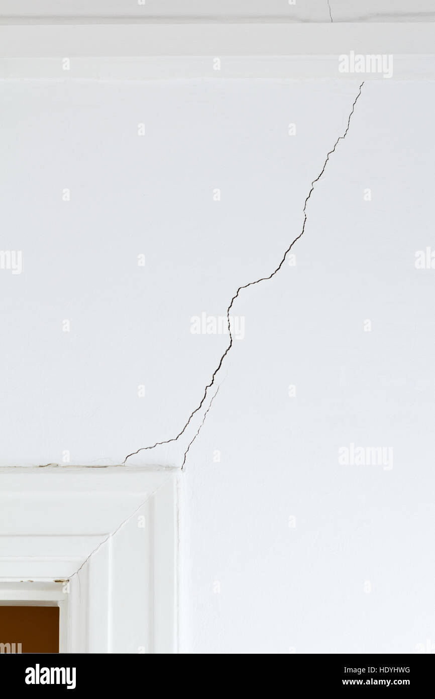 White wall and door case in an old house with a long crack or rip, structural damage Stock Photo