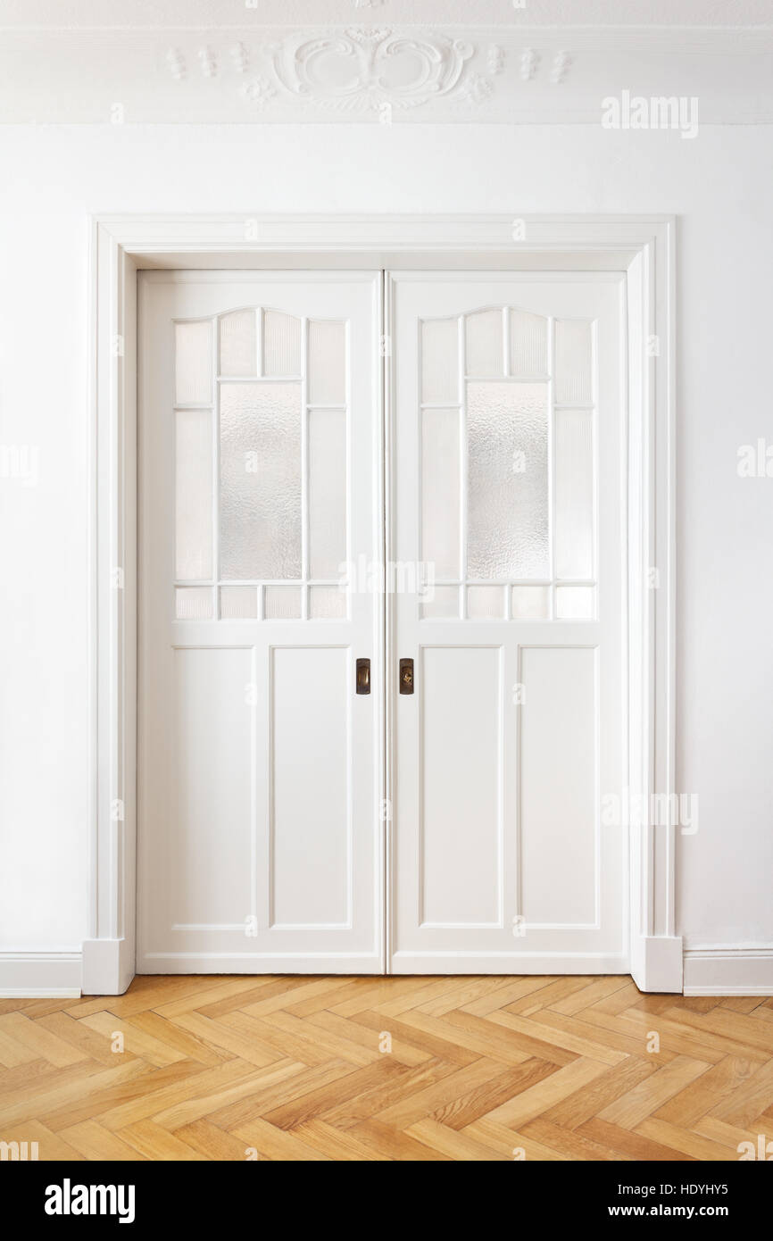 Nostalgic old double sliding door with textured glass in an historic building with stucco on the ceiling, white wall, parquet Stock Photo