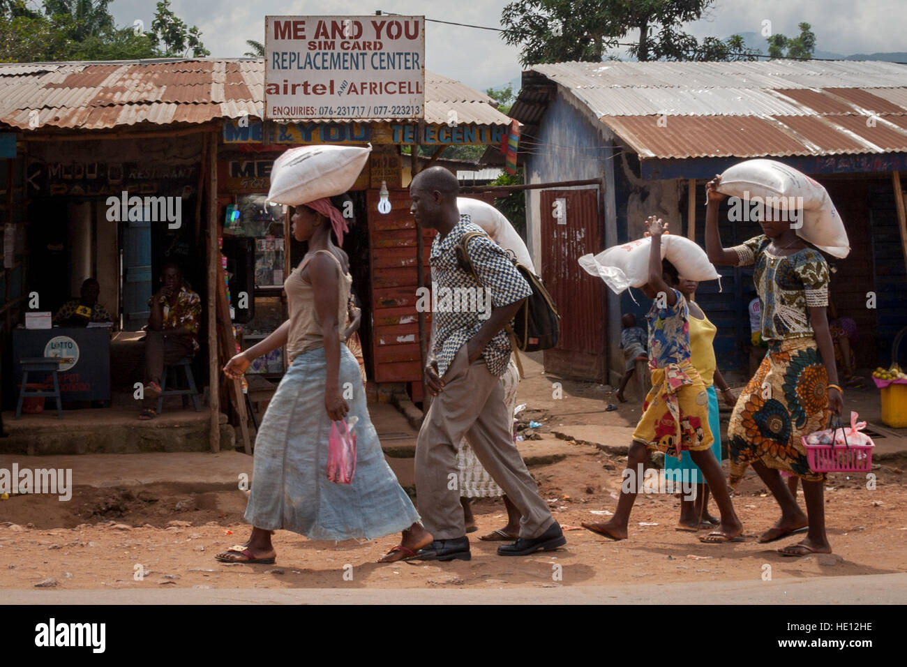 Mother and daughters in Sierra Leone carrying heavy bags of cereals on their head Stock Photo