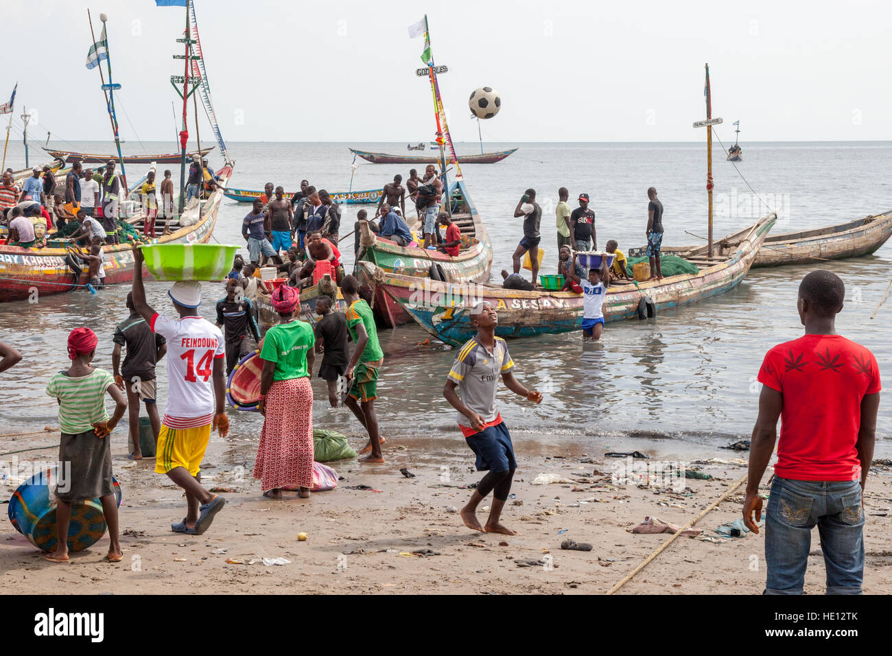 Busy traffic on beach in Tombo Harbour, Sierra Leone. The port of Tombo has no basin. It is a beach, 40 kilometers from Sierra Leone's capital Freetown. From here 700 fishing boats go out to sea. Young men carrying heavy bowls of fish from boat to shore. Others play football while waiting for more boats to arrive. Stock Photo