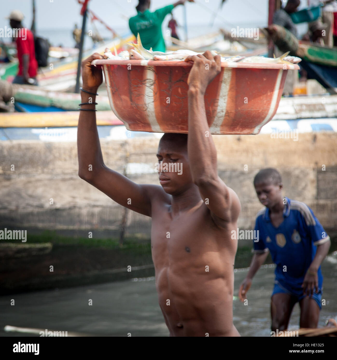 Young african man carrying big bowl of fish from ship to shore Stock Photo