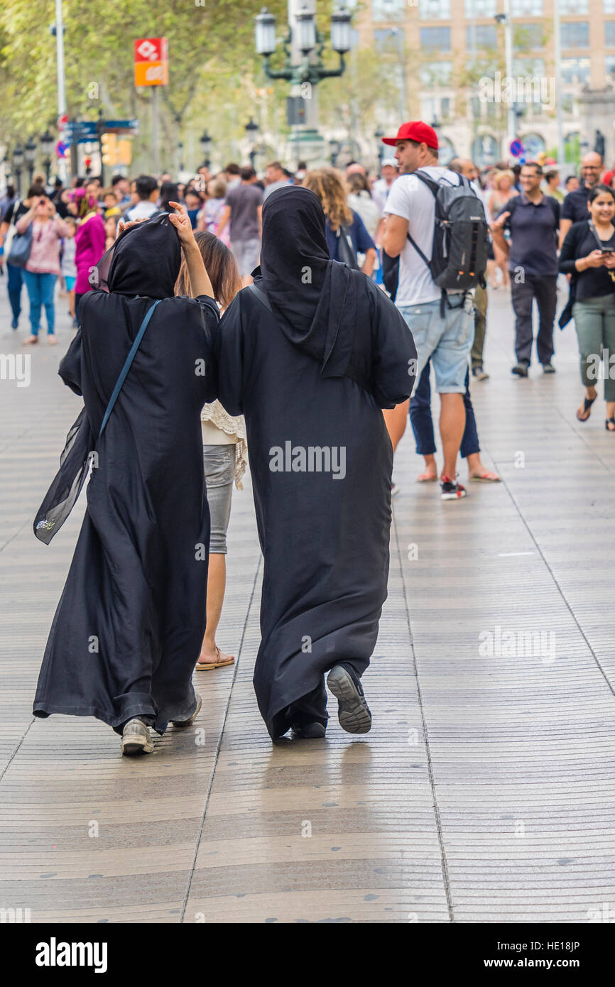 Two Muslim women wearing black colored burkas walk together along the famous walking street La Rambla in Barcelona, Spain. Stock Photo
