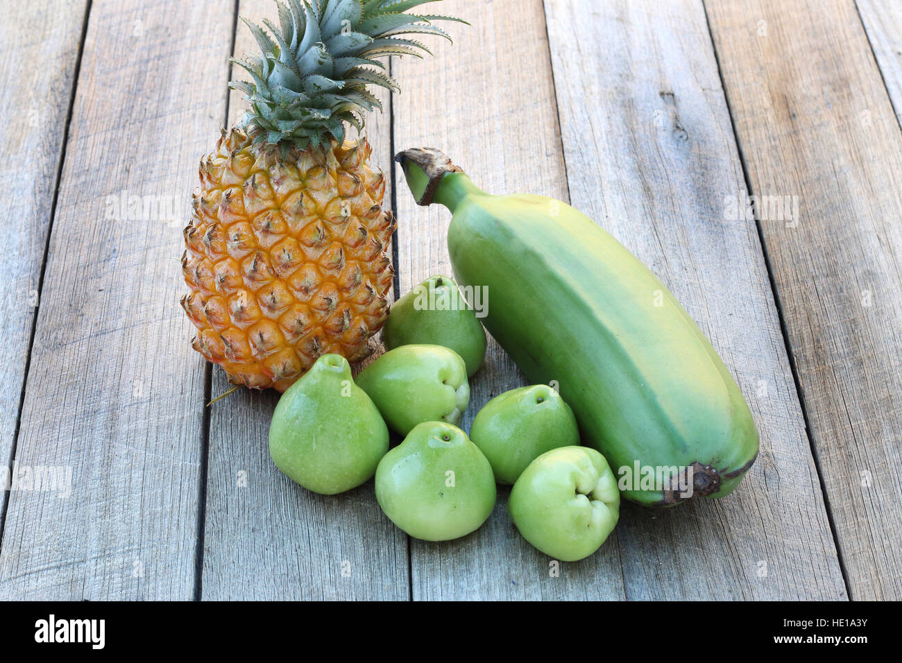 Tropical fruits pineapple, plantain banana and rose apple on timber