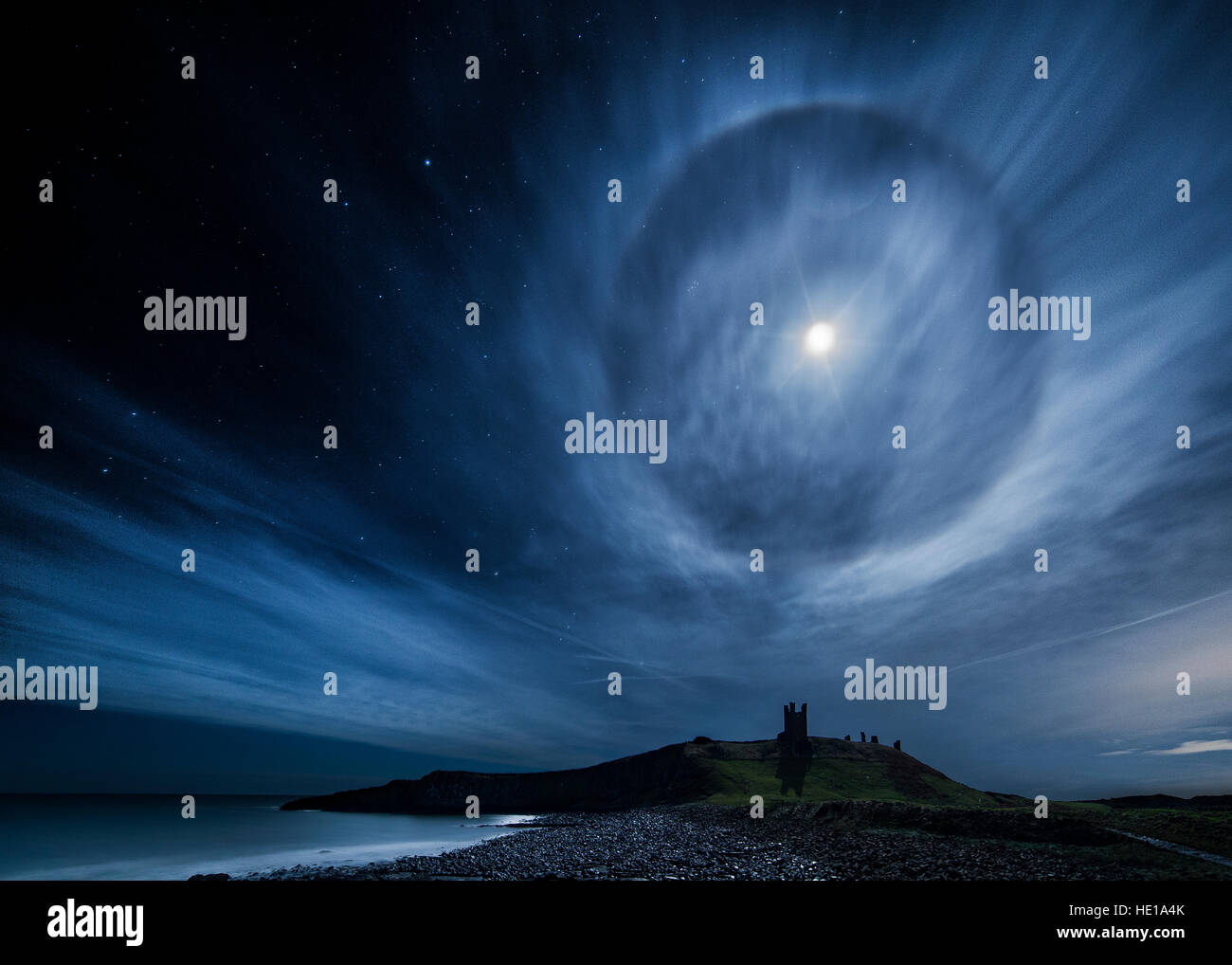 A 22° lunar halo over Dunstanburgh Castle on Northumberland coast in the UK Stock Photo