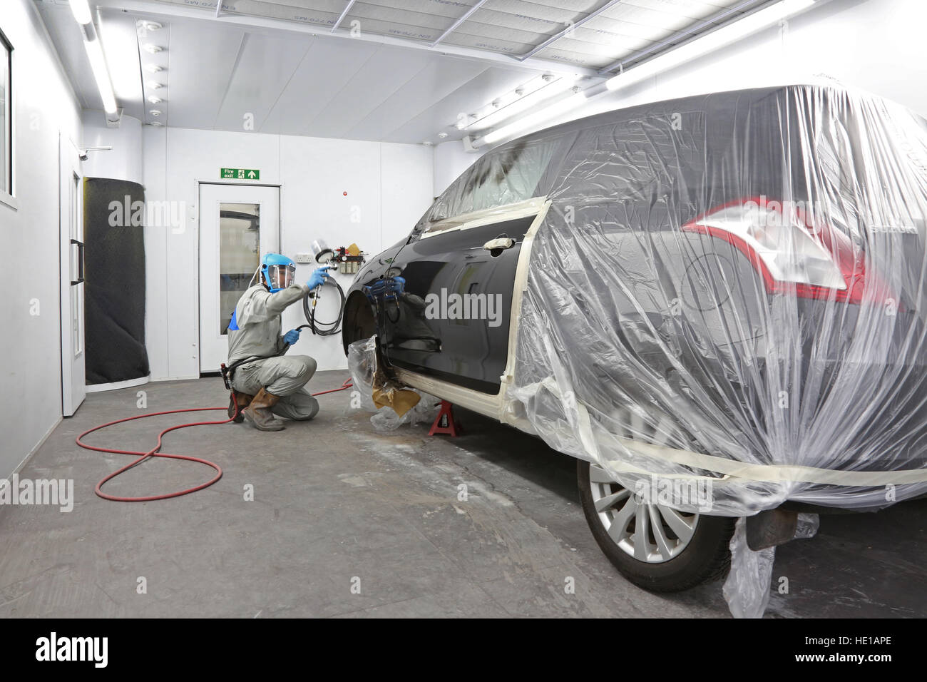 A mechanic in a modern body repair shop uses a compressed air spray gun to repaint side panels on a repaired car Stock Photo