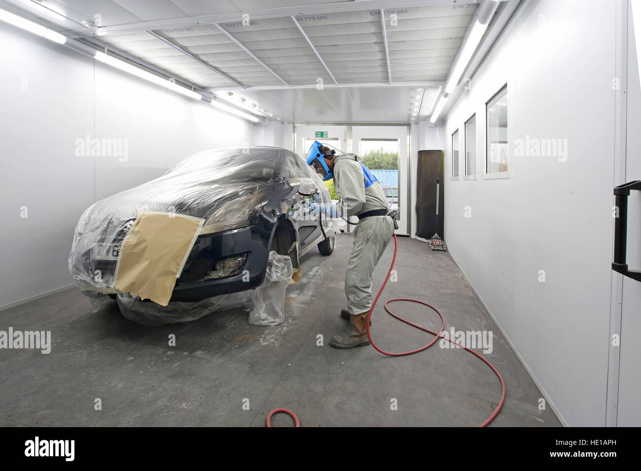 A mechanic in a modern body repair shop uses a compressed air spray gun to repaint side panels on a repaired car Stock Photo