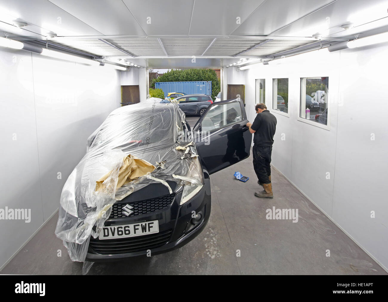 A mechanic in a car body repair shop removes masking after painting (numberplate numbers changed) Stock Photo