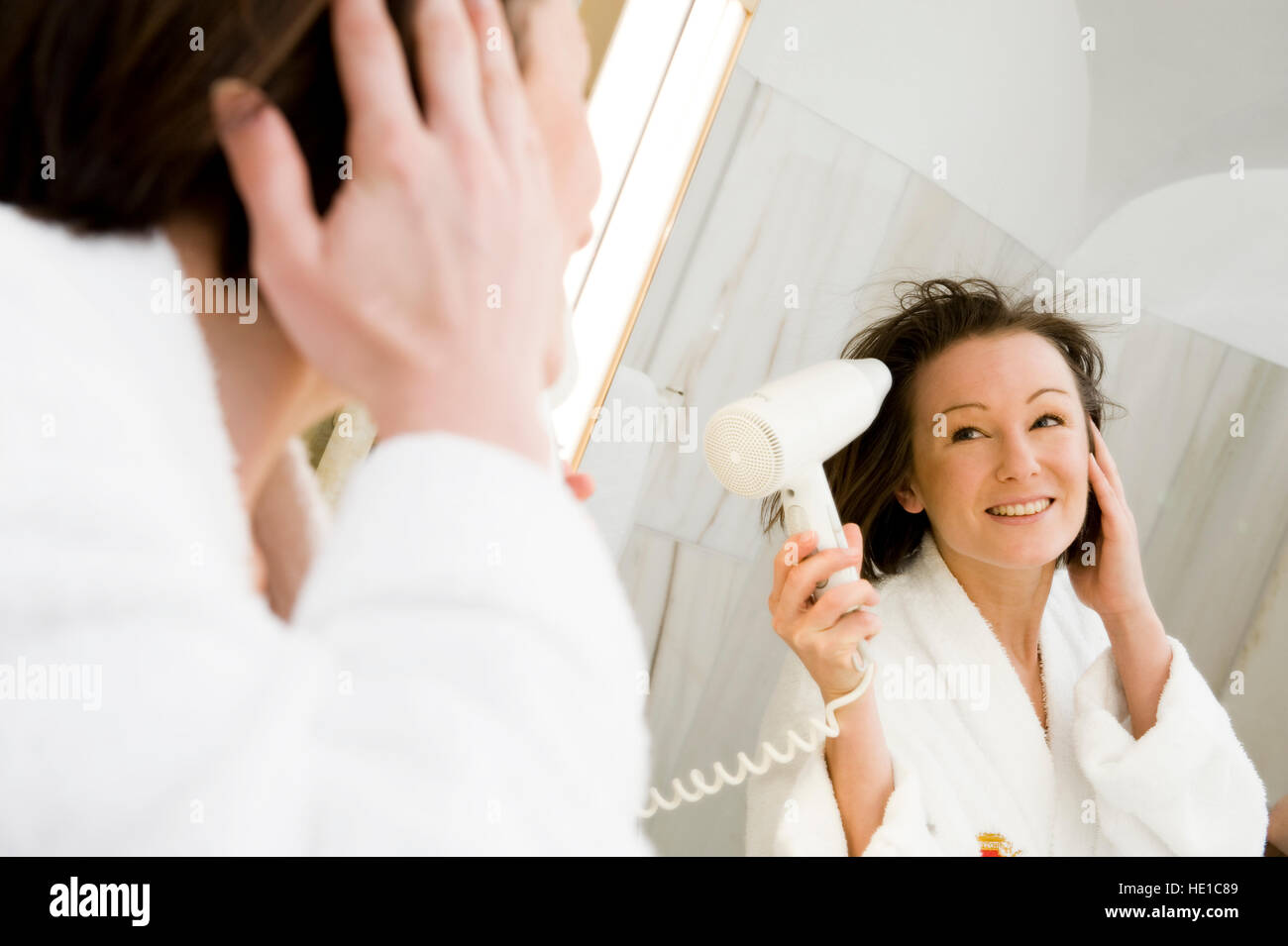 Young woman blow drying her hair in the bathroom Stock Photo - Alamy