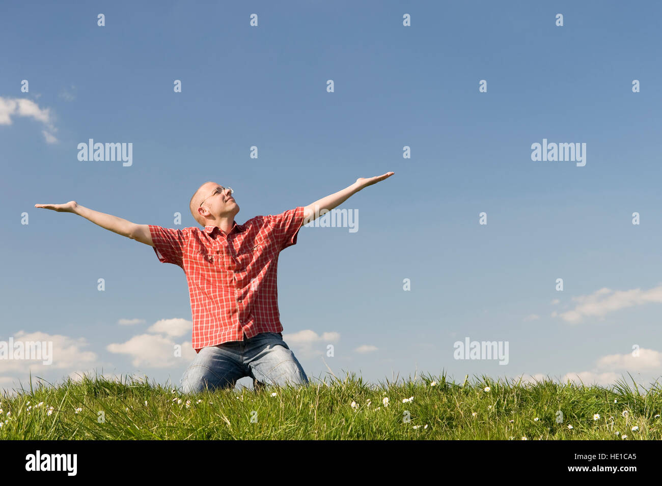 Young man kneeling on a meadow with outstreched arms Stock Photo