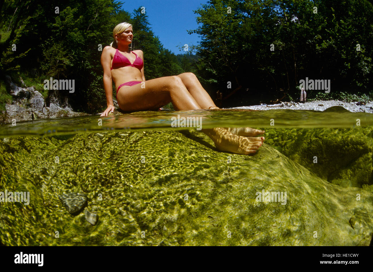 21-year-old woman sitting on a rock in a mountain stream resting her feet in the water, Reichraming, Upper Austria, Austria Stock Photo