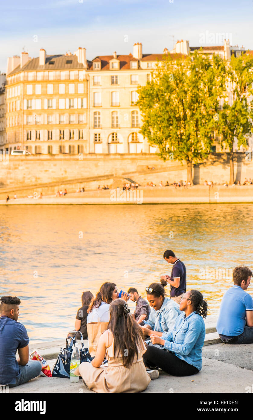 young people having a picnic on the banks of river seine at dusk Stock