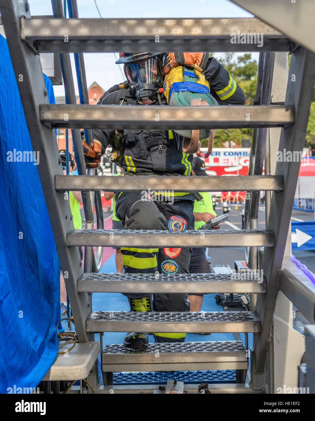 A firefighter starts up stairs on a four story tower carrying bundled hose. Stock Photo