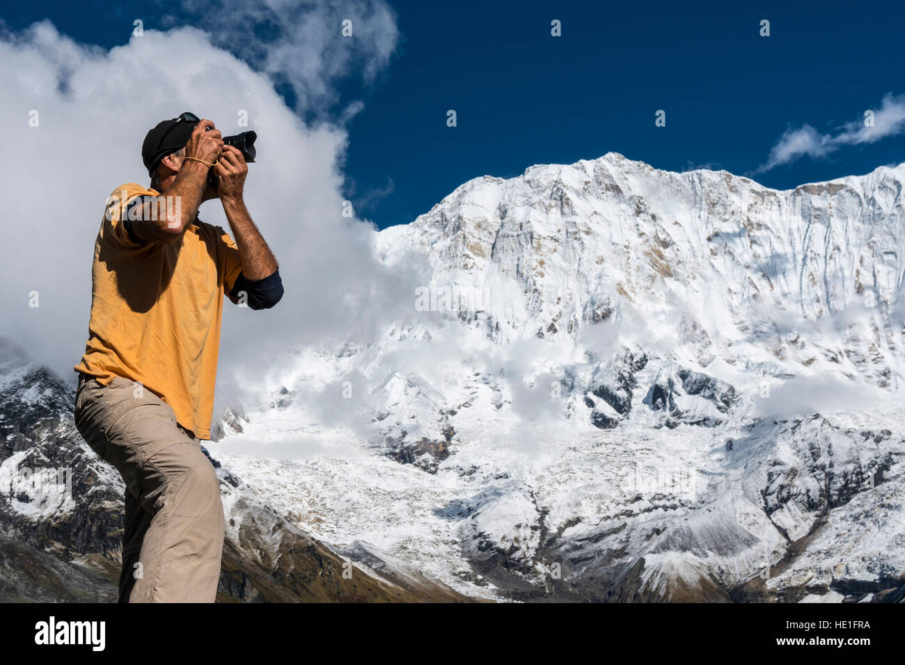 A photographer is taking a picture of the barren landscape of Annapurna Base Camp, the snow covered Annapurna 1 North Face in the distance Stock Photo