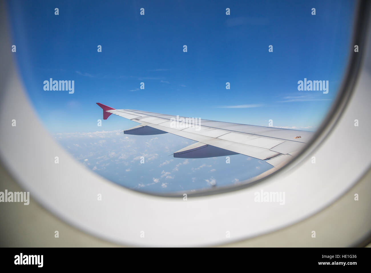 View through a window of an left airplane wing aircraft flying above the clouds in a blue sky. Stock Photo
