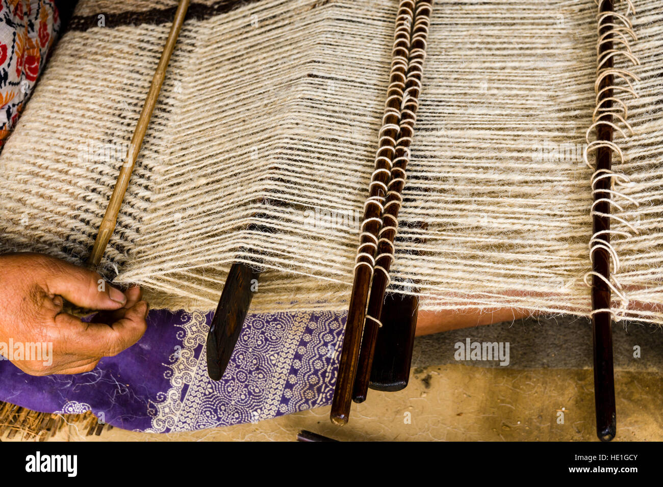 A local woman is weaving a blanket, using sheep wool, in front of a