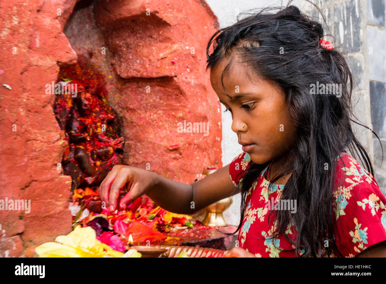 A little girl is offering prasad to the statues of gods outside the temple Khadga Devi Mandir at the hinduist festival Darsain Stock Photo