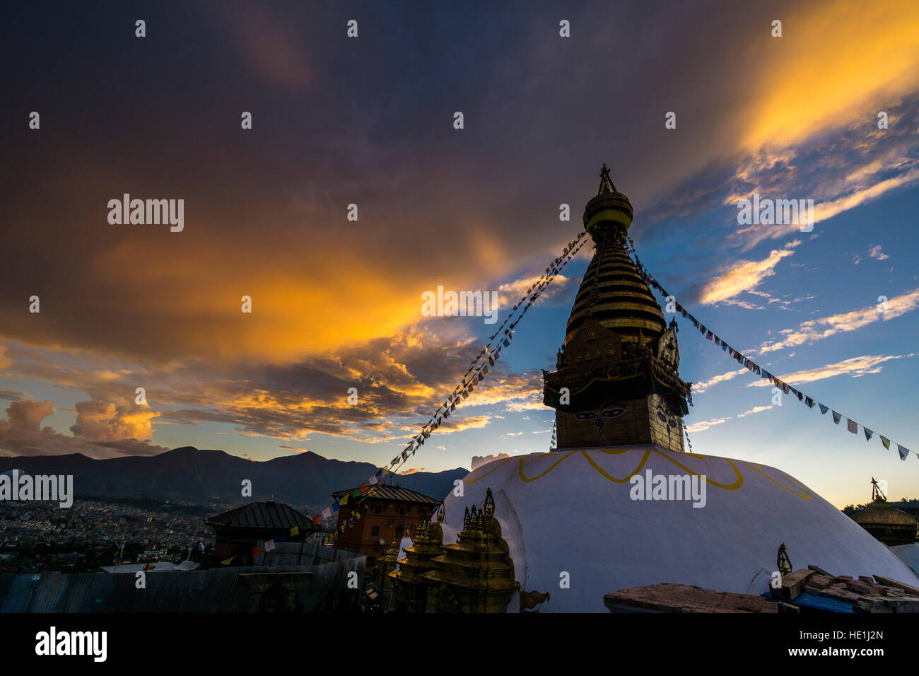 The white stupa of Swayambhunath temple, Monkey Temple, is decorated with tibetan prayer flags, big orange sunset clouds above Stock Photo