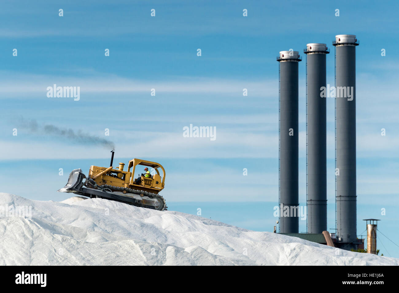 An earth mover (Bulldozer) piles road salt that has just been offloaded from a ship. The salt will be used to deice frozen roads Stock Photo