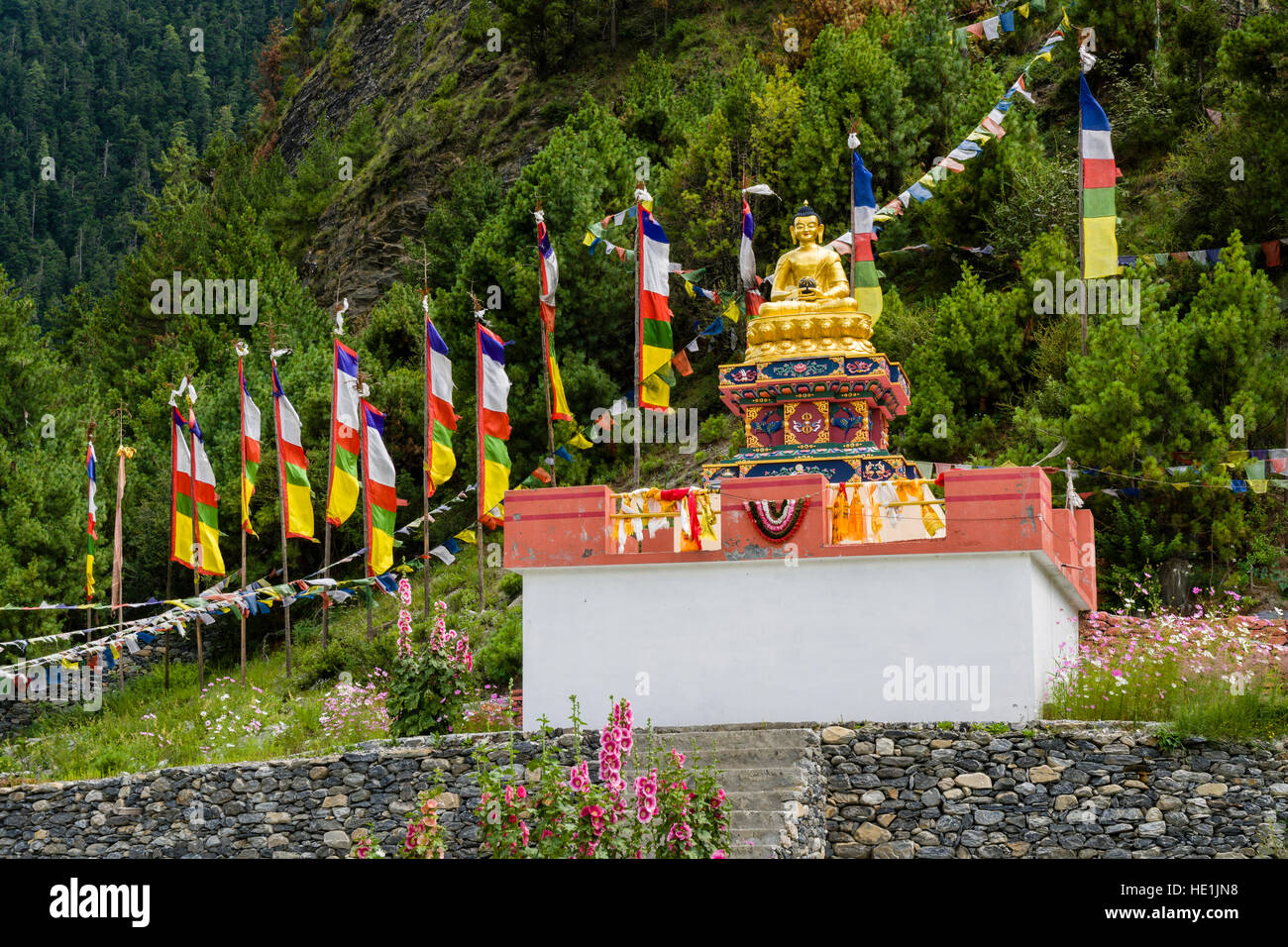 A golden Buddha statue is set on a stone base, surrounded by prayer flags Stock Photo