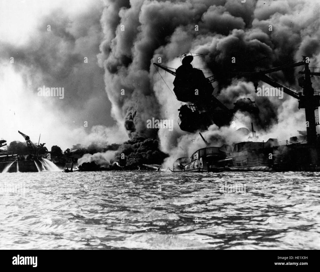 USS Arizona BB-39 sunk and burning furiously, 7 December 1941. Her forward magazines had exploded when she was hit by a Japanese bomb. At left, men on the stern of USS Tennessee BB-43 are playing fire hoses on the water to force burning oil away from their ship Official U.S. Navy Photograph, now in the collections of the National Archives. Stock Photo
