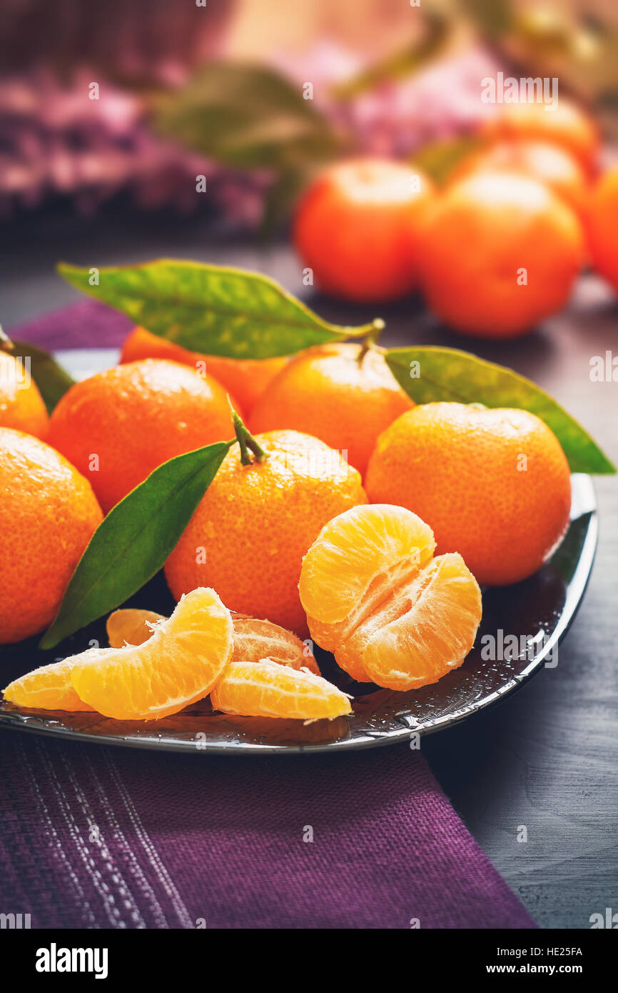 Fresh clementines with leaves served on plate, on black wooden table Stock Photo