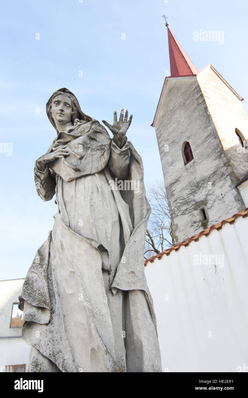 Granite statue of Virgin Mary with church tower Stock Photo Alamy