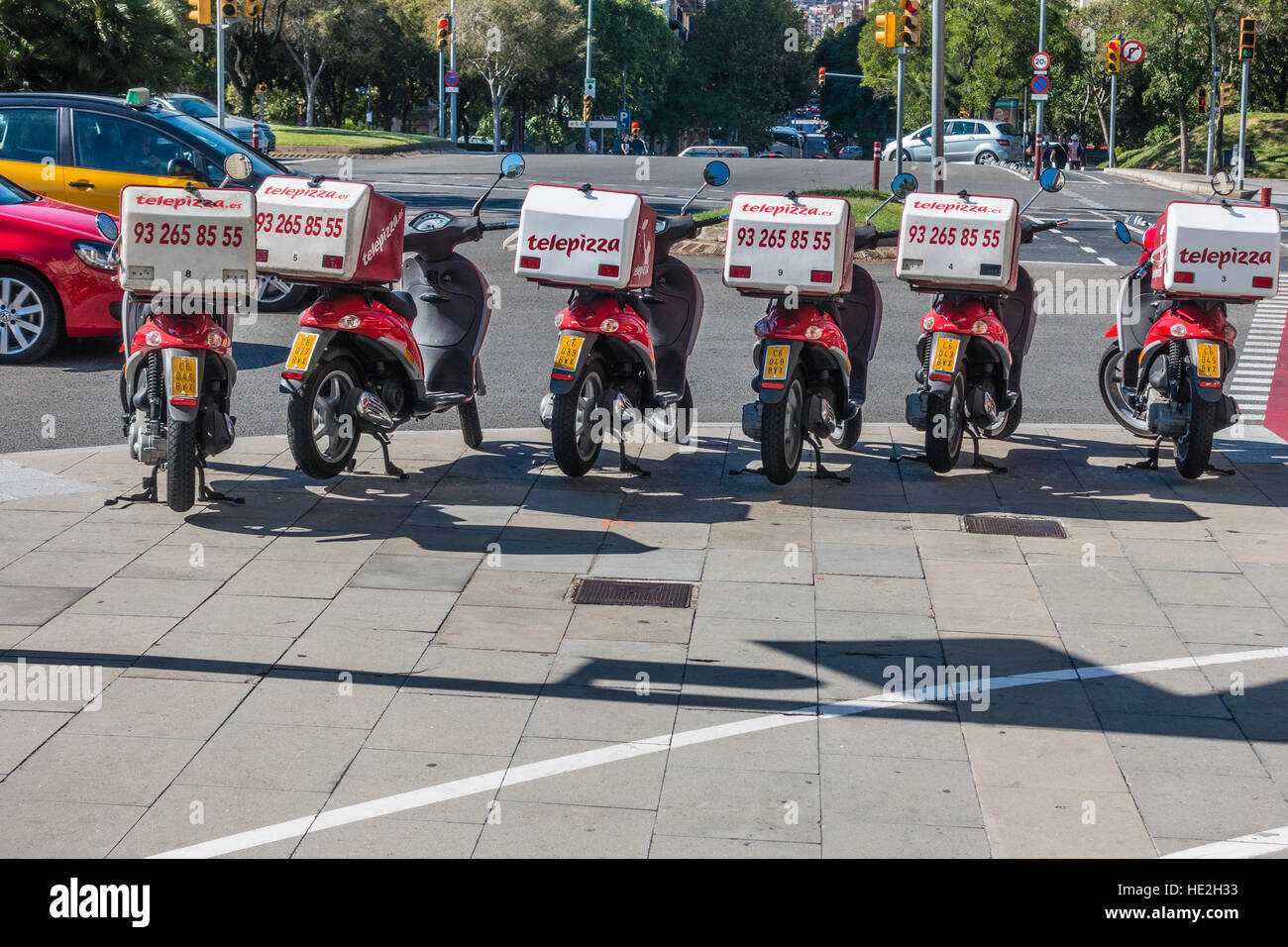 A line of Telepizza motoscooters parked on a sidewalk in Barcelona, Spain with their delivery boxes attached to their backs. Stock Photo