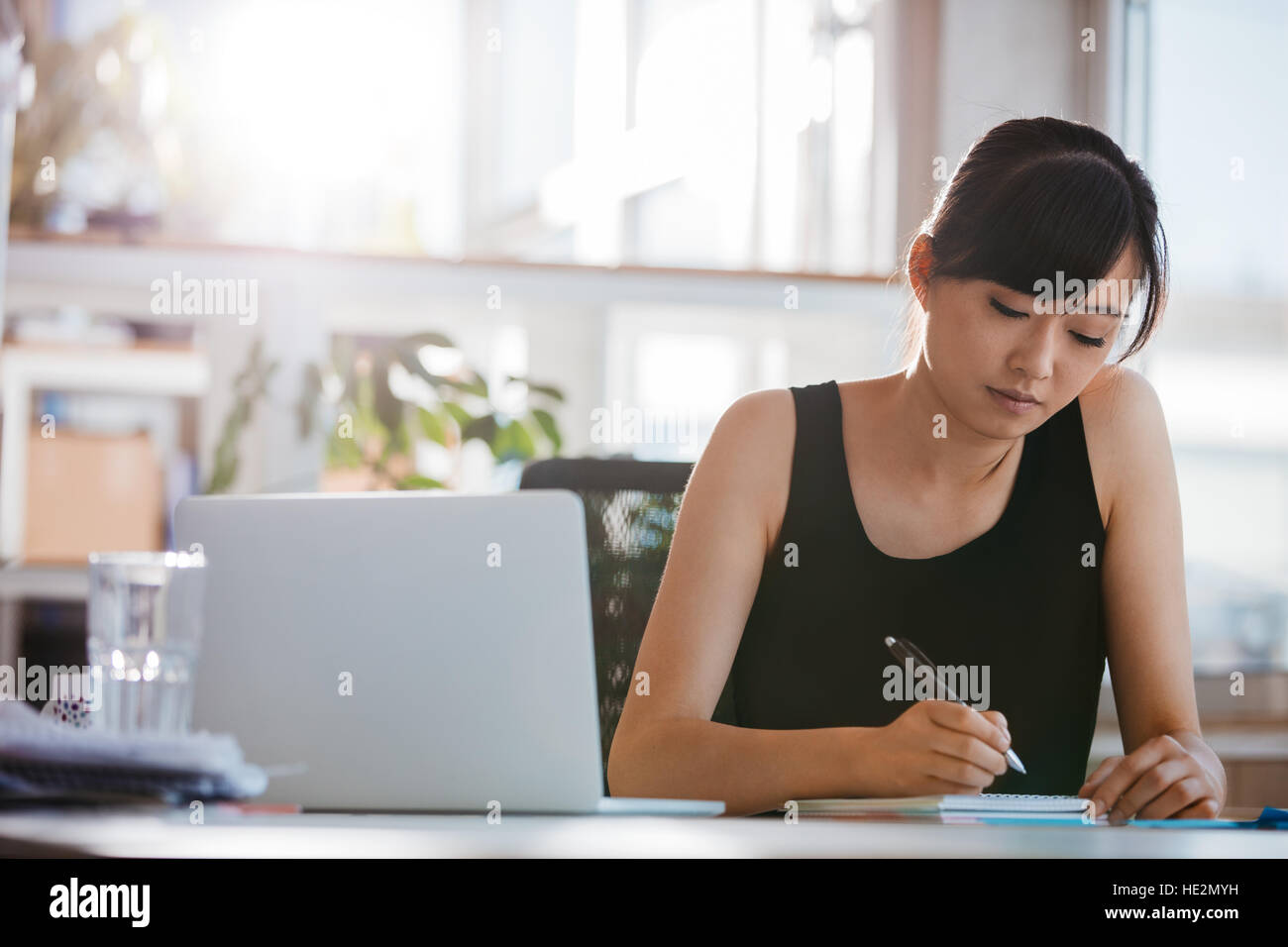 Shot of young woman sitting at a table and writing notes. Businesswoman working at her desk. Stock Photo