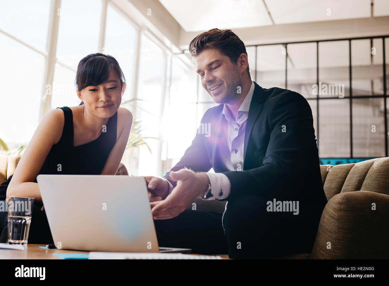 Shot of two young businesspeople using laptop in lobby of modern office. Man and woman sitting on foyer working together on laptop. Stock Photo