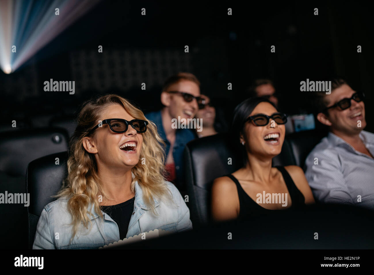 Group of friends watching 3d movie and laughing in cinema. Happy young men and women watching 3d film in theater. Stock Photo