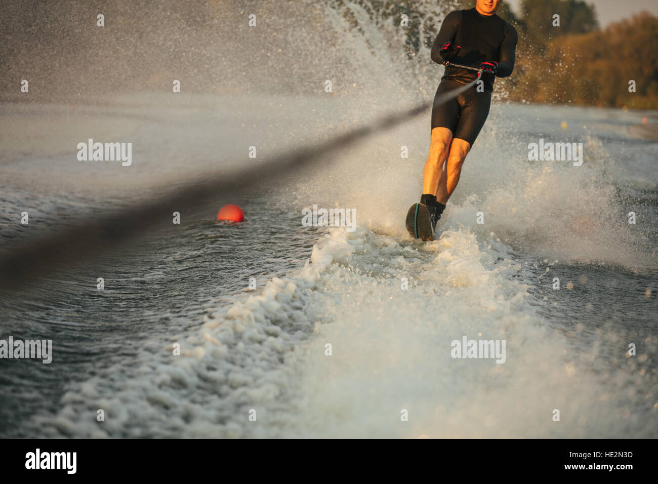 Man riding wakeboard on wave of motorboat in a lake. Male water skiing behind a boat. Stock Photo